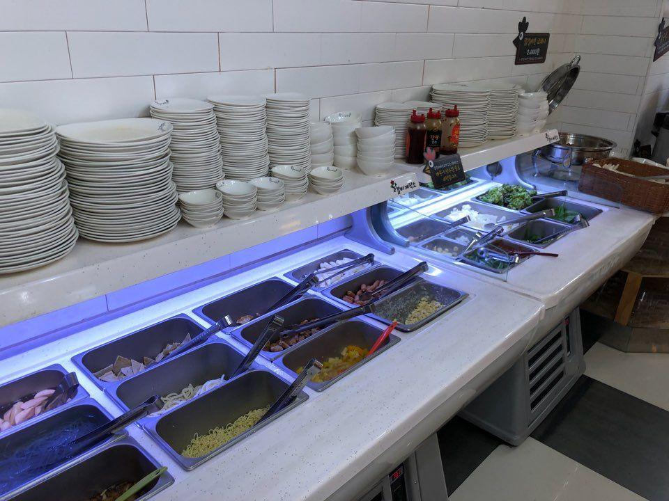 A well-organized buffet counter featuring ingredients for Dakgalbi, with neatly stacked plates and various food trays exuding Korean culinary style.